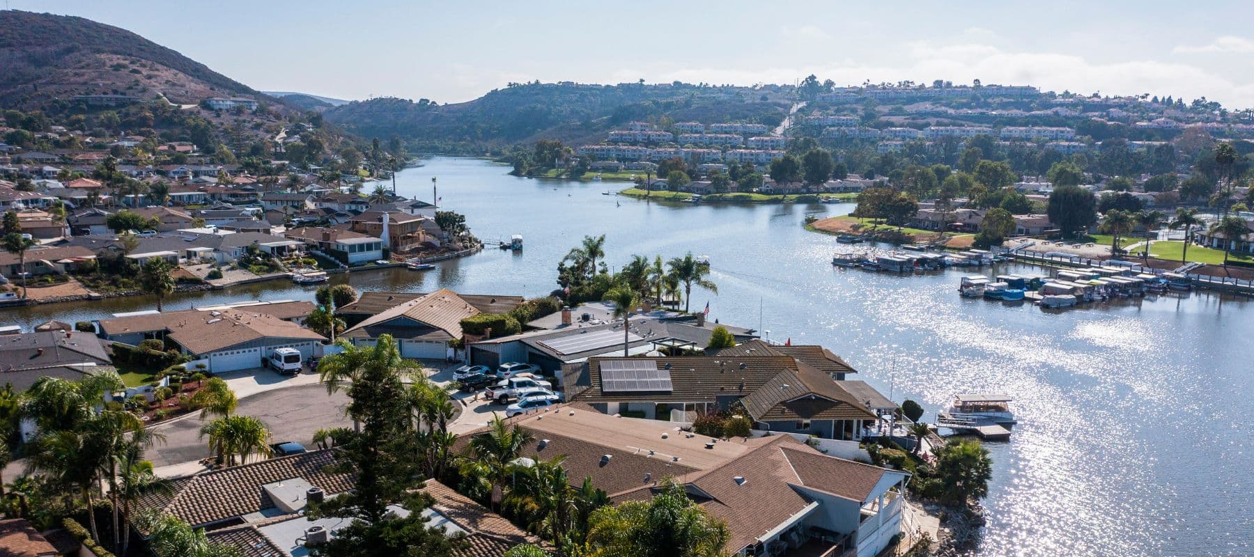 Aerial view of a lakefront neighborhood with docks, homes, and hills in the background