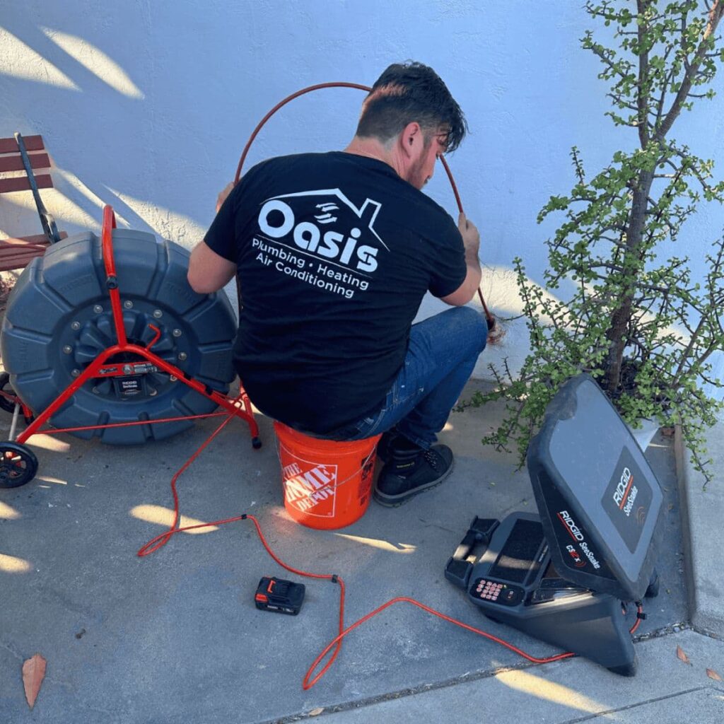 Oasis technician using a pipe inspection camera and drain auger setup on a concrete driveway