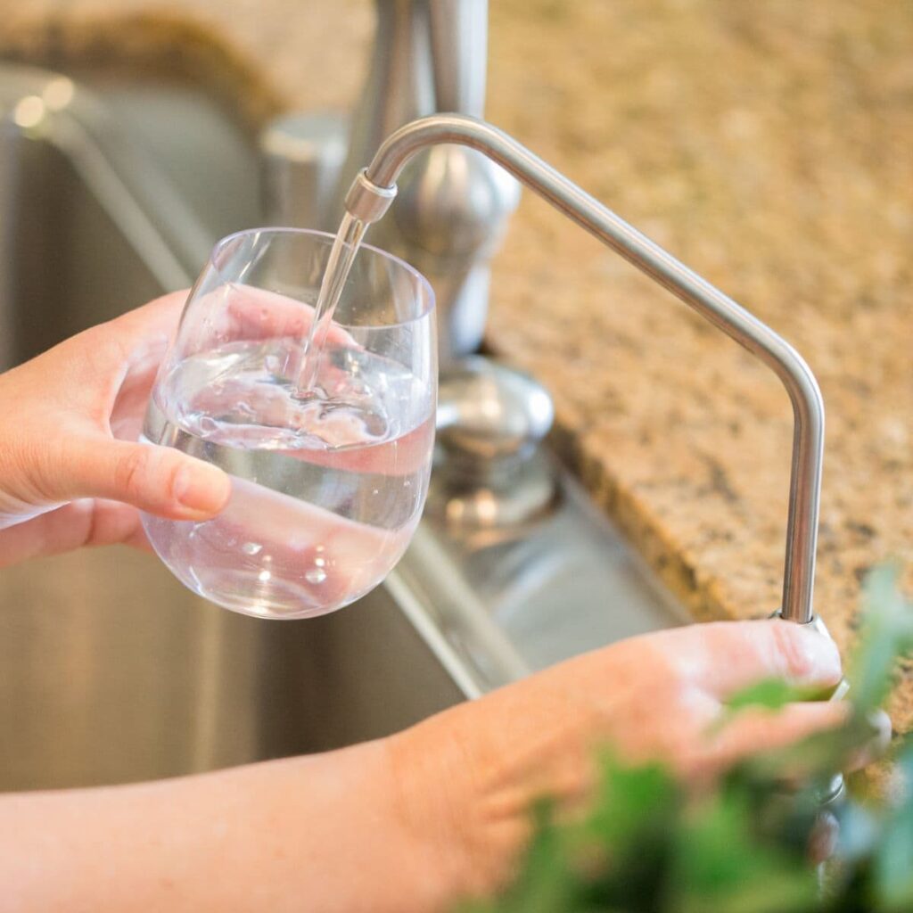 Glass being filled with water from a sleek kitchen filtration faucet