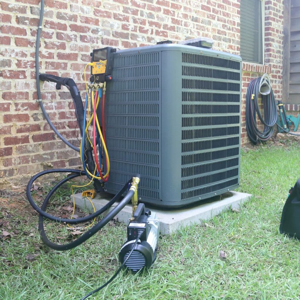 Air conditioning unit undergoing maintenance with attached gauges and vacuum pump on a lawn