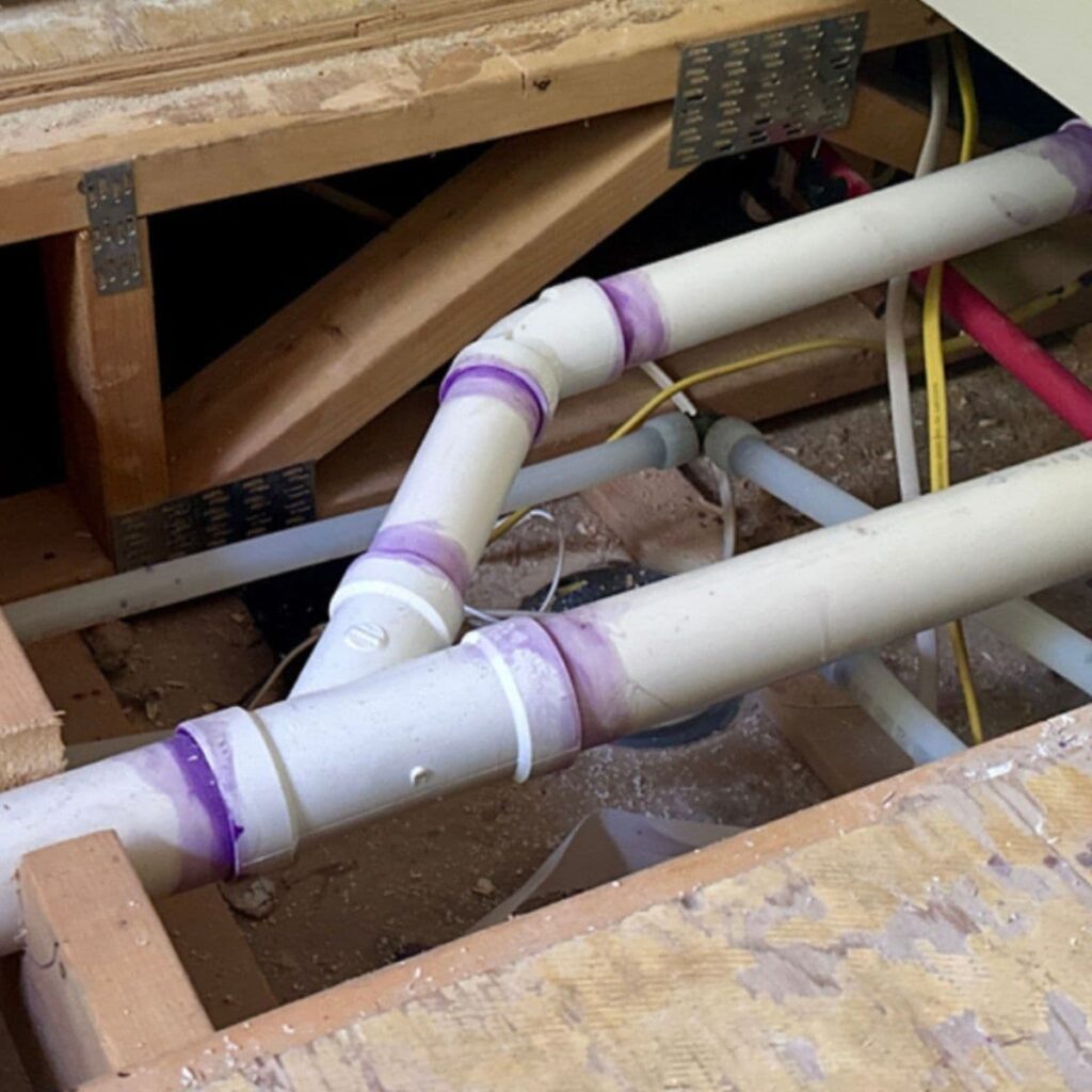 Network of white PVC pipes with purple primer fittings installed through attic joists
