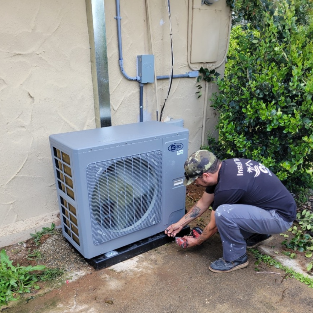 HVAC technician in camo hat installing an outdoor mini split condenser unit