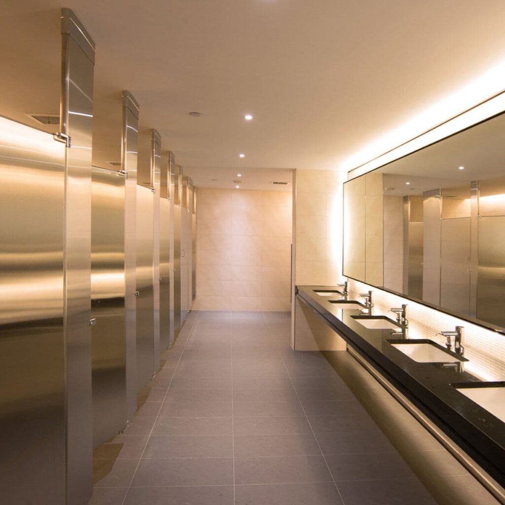 Sleek, modern commercial bathroom interior with stainless steel stalls and underlit sinks