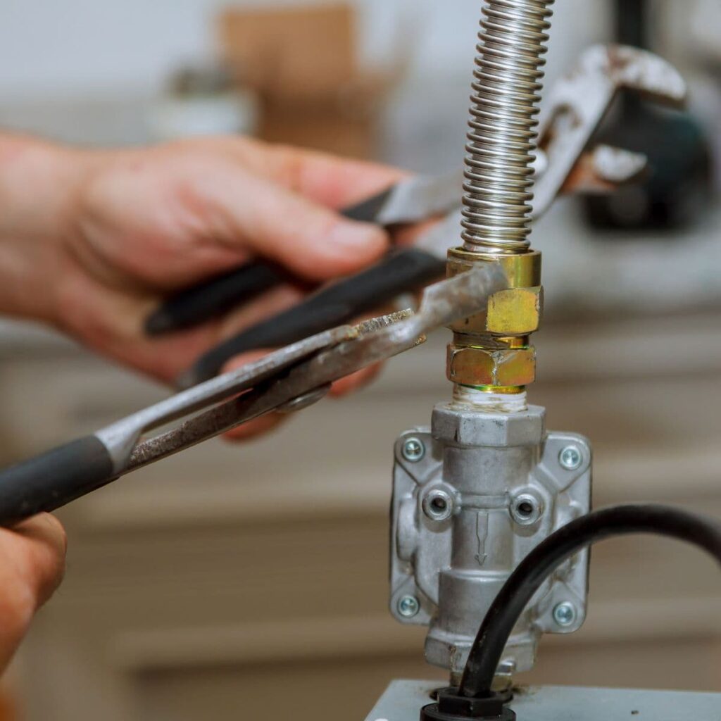 Close-up of a plumber using two wrenches to tighten a flexible gas line fitting