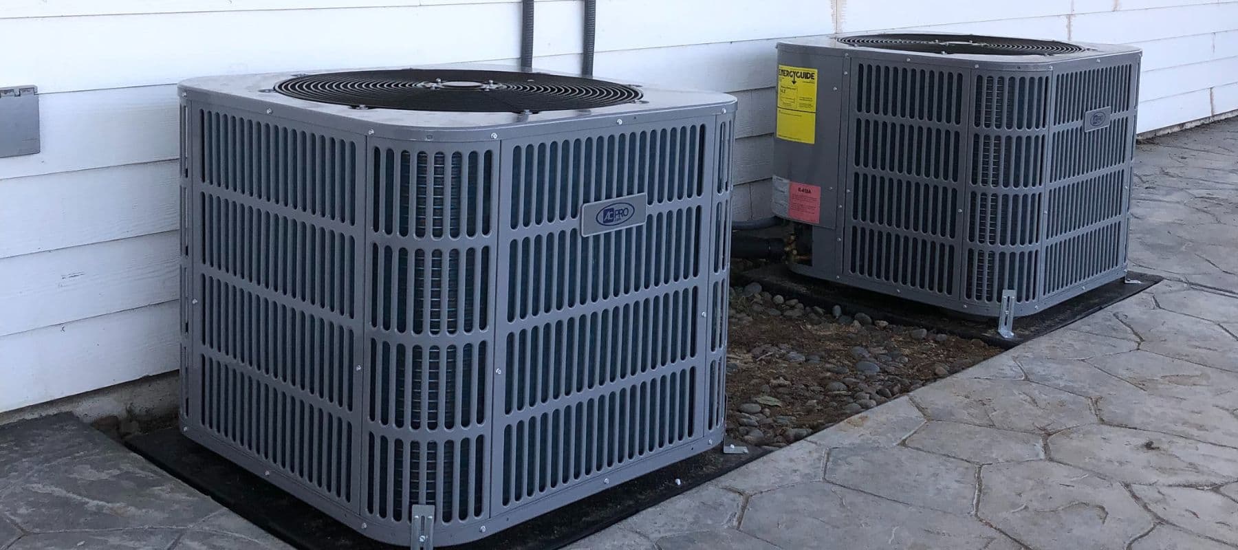 Two AC Pro brand air conditioning condensers installed next to a home's exterior wall