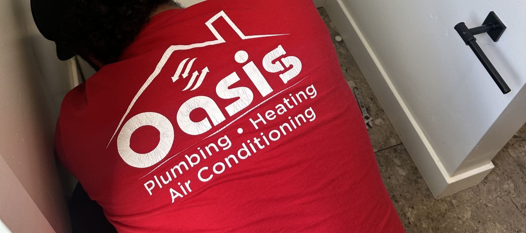 Oasis Plumbing technician working behind a toilet in a small bathroom space