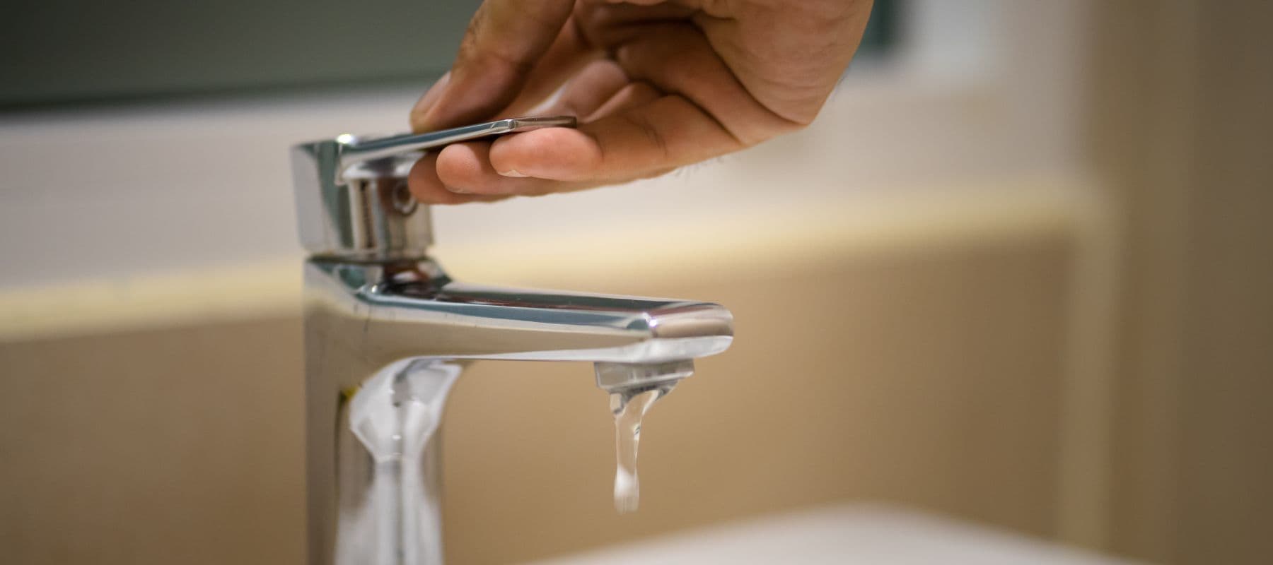 Hand turning on a modern bathroom faucet with weak water flow