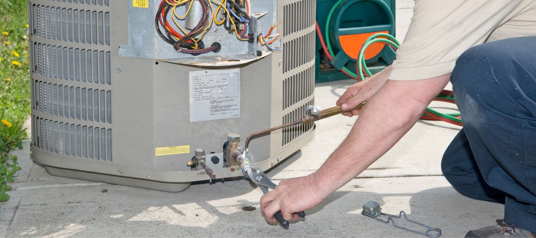 Technician welding refrigerant lines on an exposed AC condenser unit