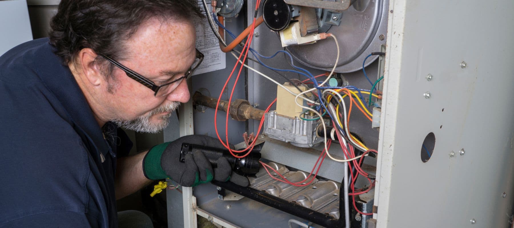 Technician using a flashlight to inspect and service internal components of a furnace
