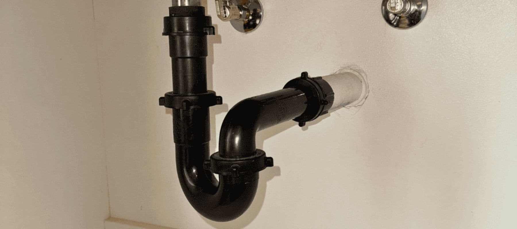 Black plastic P-trap plumbing connection under a sink