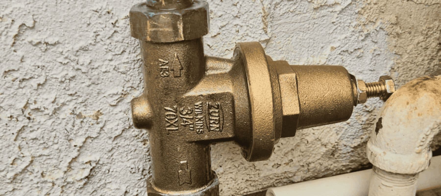 Close-up of a brass pressure-reducing valve attached to an exterior water line
