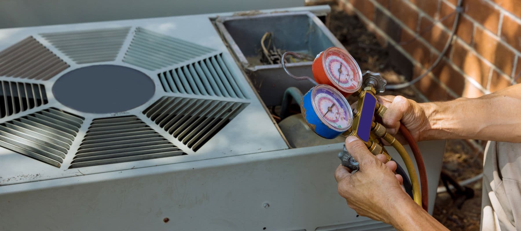 Technician using HVAC pressure gauges to check an open air conditioner unit