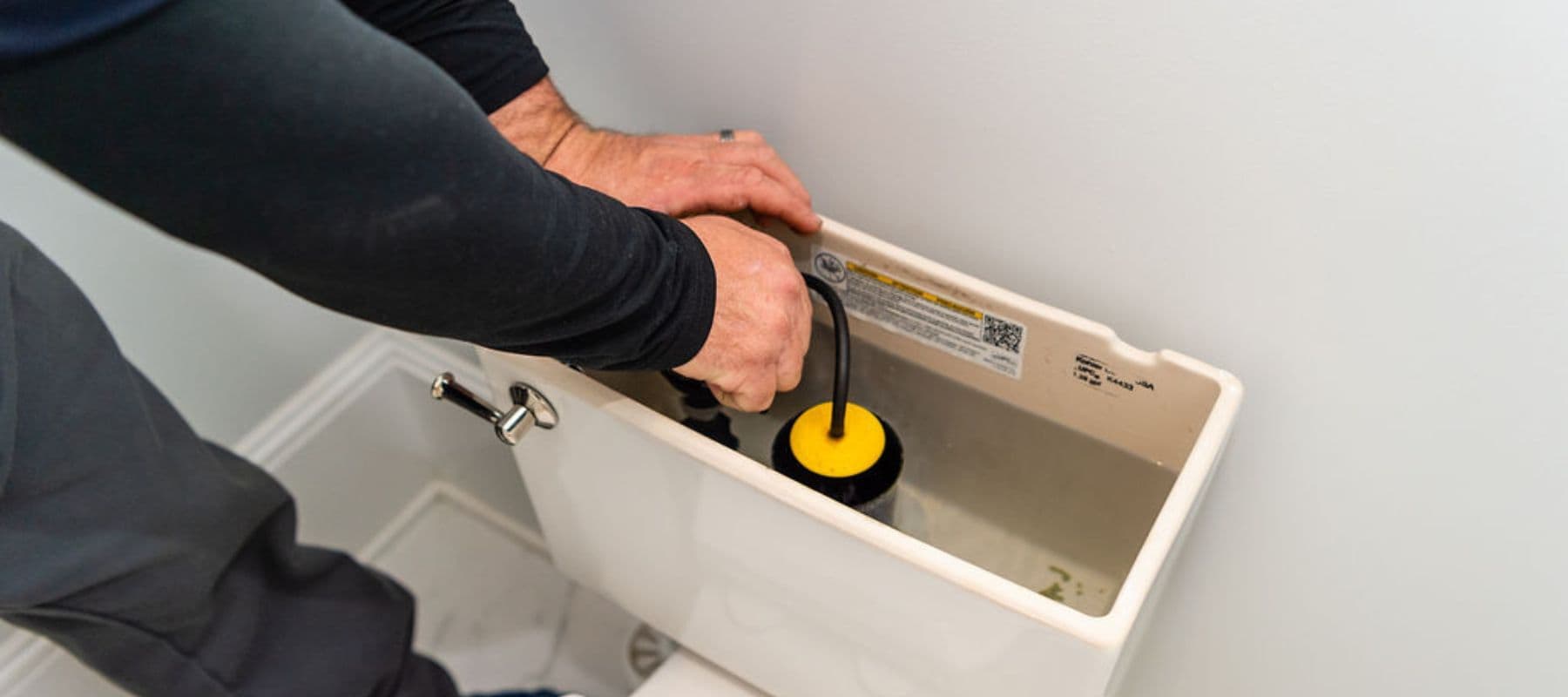 Technician inspecting and adjusting components inside a toilet tank