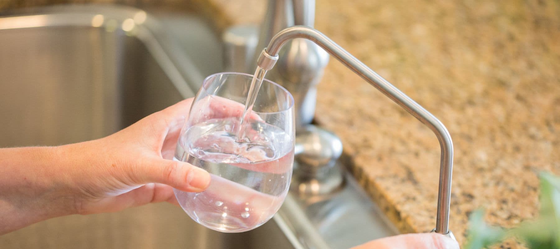 Glass being filled with water from a sleek kitchen filtration faucet