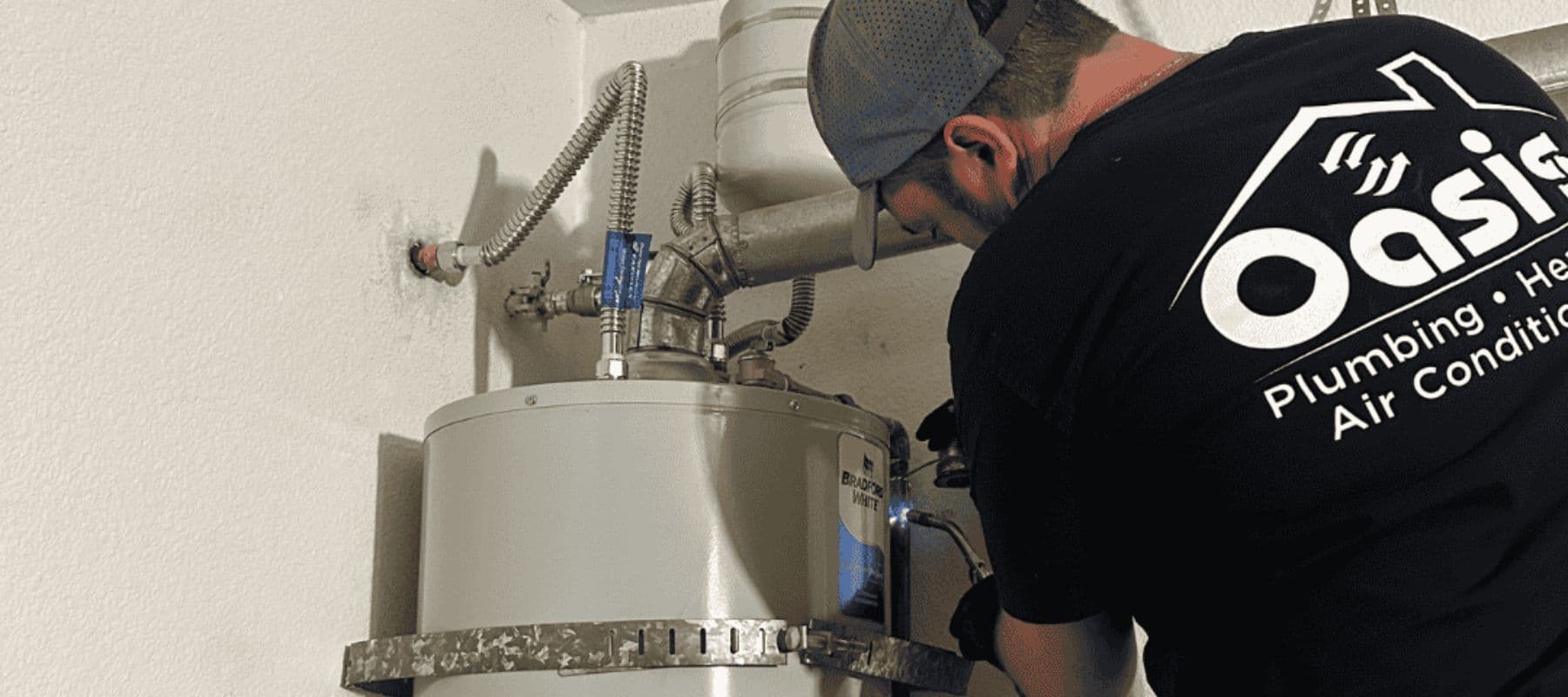 Technician from Oasis Plumbing working on a water heater inside a utility space