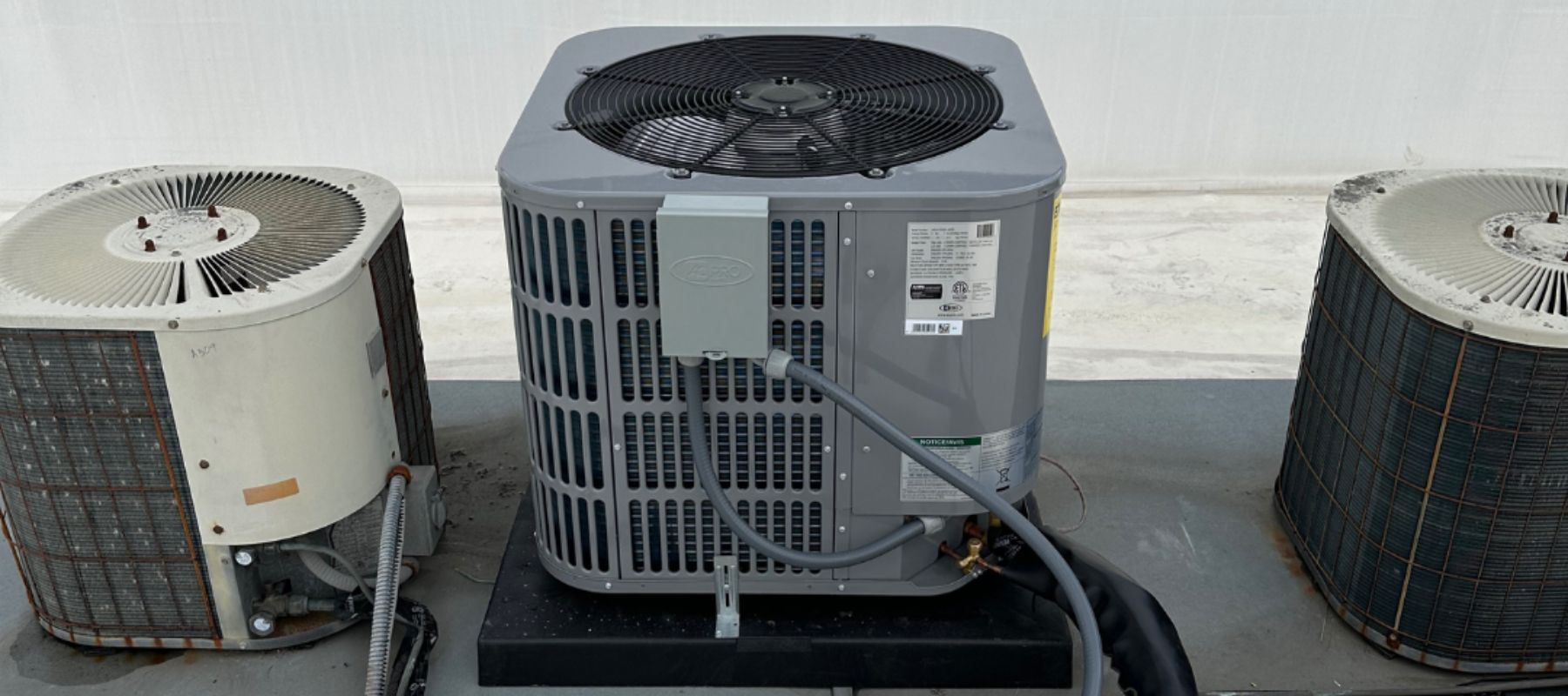 Three HVAC condenser units on a flat rooftop, including a newer gray model in the center