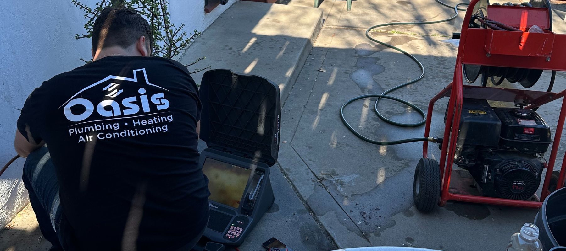 Technician in an Oasis Plumbing shirt using video inspection equipment near a sewer line setup